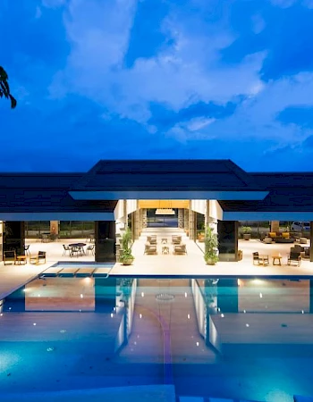 The image shows a luxurious outdoor swimming pool at dusk, with a modern building and ambient lighting in the background.