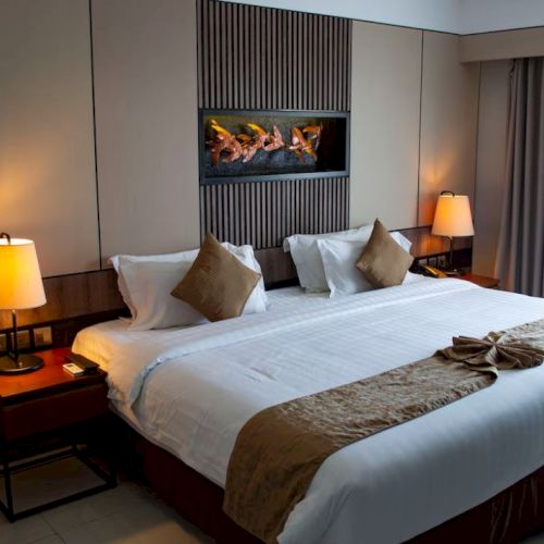 The image shows a modern hotel bedroom with a large bed, two bedside tables, two lamps, and a decorated wall niche.