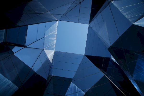 The image shows a geometric architectural structure with reflective glass panels, creating an abstract pattern against a blue sky backdrop.
