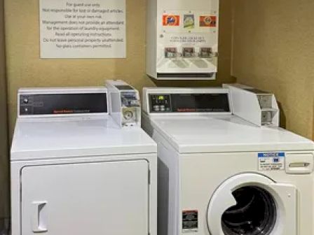 A laundry room with a washer, dryer, detergent dispenser, and a sign reading 