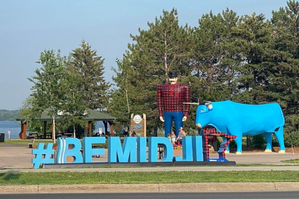 A statue of a lumberjack and a large blue ox stands behind large hashtag 