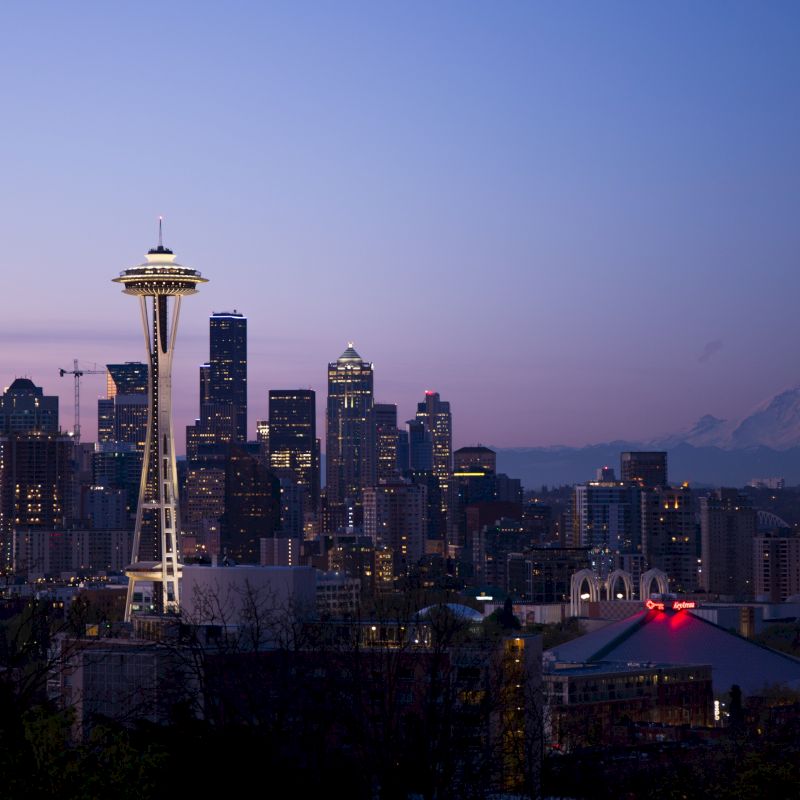 The image showcases the Seattle skyline at dusk, featuring the Space Needle prominently with Mount Rainier visible in the background.