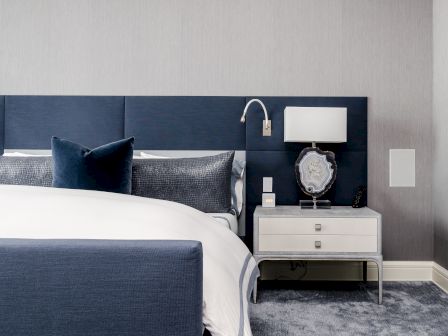 A modern bedroom with a blue and white color scheme, featuring a bed with blue headboard and pillows, and a nightstand with a lamp and decorative item.