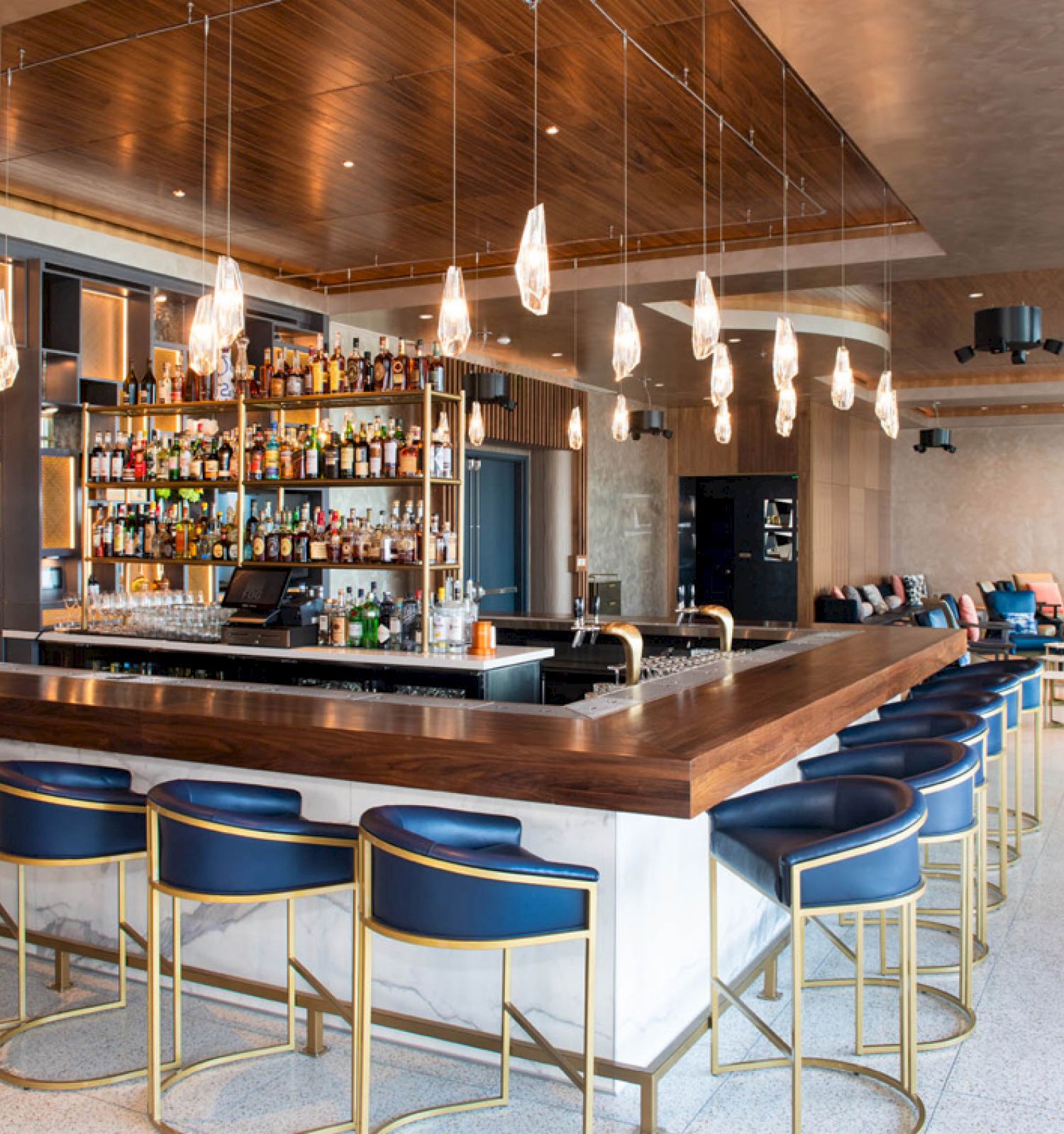 This image shows a modern bar with a sleek design, featuring a large counter, stylish bar stools, hanging lights, and a well-stocked liquor shelf.